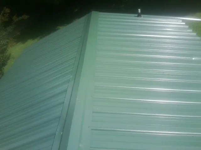 New green metal panels meeting at the ridge of a roof — Flat Roof Repair work by our crew in Burkeville