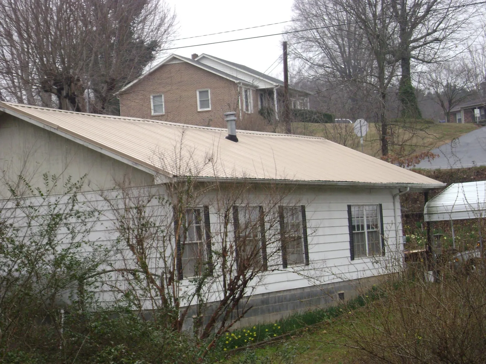 Tan metal roof on a white sided house set into a hillside — Commercial Roofing by Roofing Brothers in Burkeville